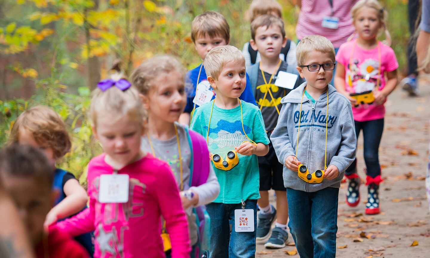 A group of children walking outdoors, each with yellow binoculars around their necks.