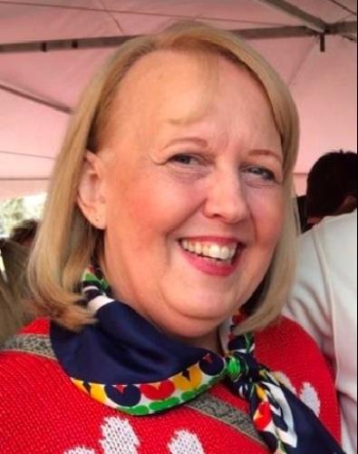 Smiling woman with blonde hair wearing a colorful scarf and a red sweater, posing under a canopy.